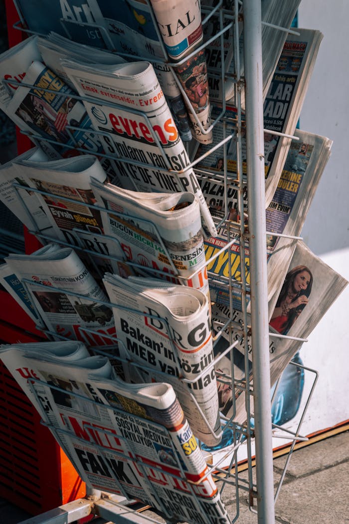 Close-up of a newspaper stand with various publications on a city sidewalk.